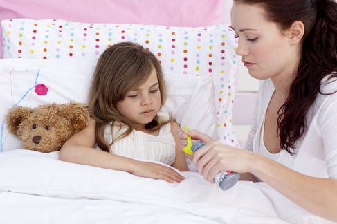 Little daughter in bed taking syrup with her mother